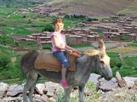 a young girl riding on a donkey near a Moroccan village