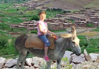 a young girl riding on a donkey near a Moroccan village