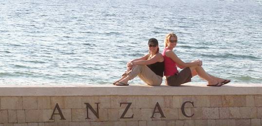 Two girls sitting on a wall at ANZAC Cove, by the sea