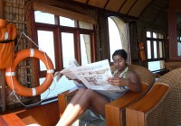 A girl relaxing and reading a paper on a house boat on the Kerala backwaters