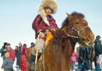 A Mongolian boy in a fur hat, on a horse