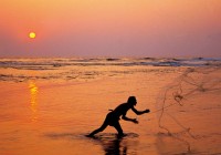 A goan fisherman using his net at sunrise