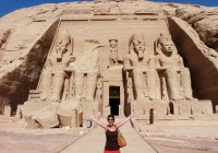 A girl outside Abu Simbel, standing in front the four colossal statues of King Ramses II