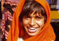 A smiling Indian girl with an orange head scarf