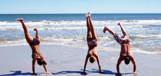 Three people doing handstands on a beach in India