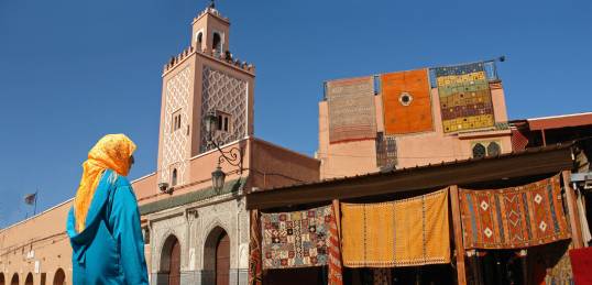 Moroccan lady and colourful rugs hanging from Marrakech's Medina walls