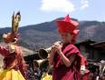 A monk from Bhutan playing a brass instrument and a brightly coloured dancer