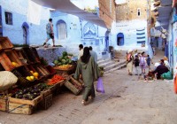 A fruit stall and Moroccan lady carrying shopping  in Chefchaouen
