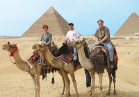 Three guys riding camels in front of the pyramids on the Giza Plateau