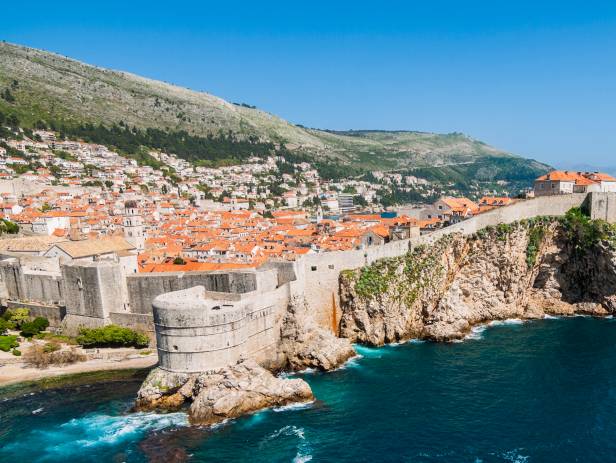 Aerial view of Dubrovnik, surrounded by water and filled with terracotta-roofed buildings