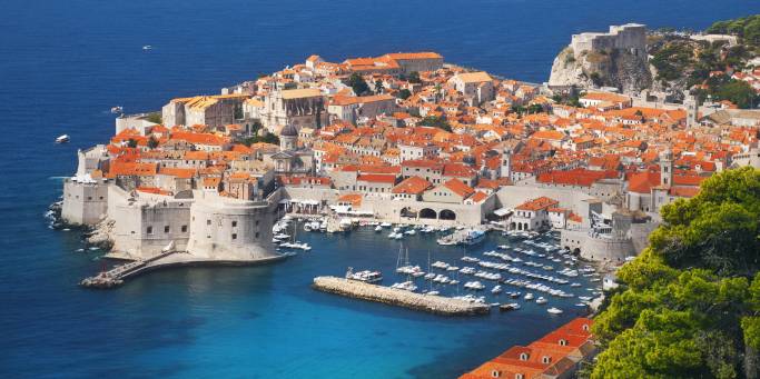 Aerial view of Dubrovnik, surrounded by water and filled with terracotta-roofed buildings