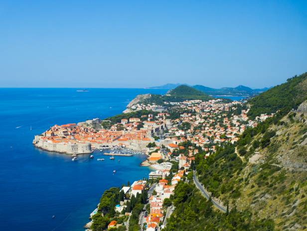 Aerial view of Dubrovnik, surrounded by water and filled with terracotta-roofed buildings