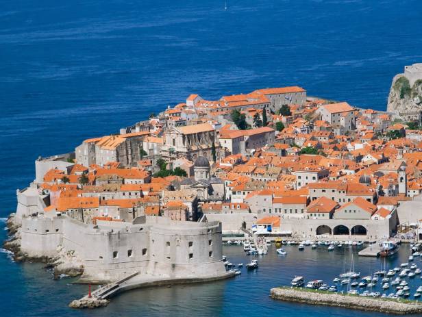 Aerial view of Dubrovnik, surrounded by water and filled with terracotta-roofed buildings