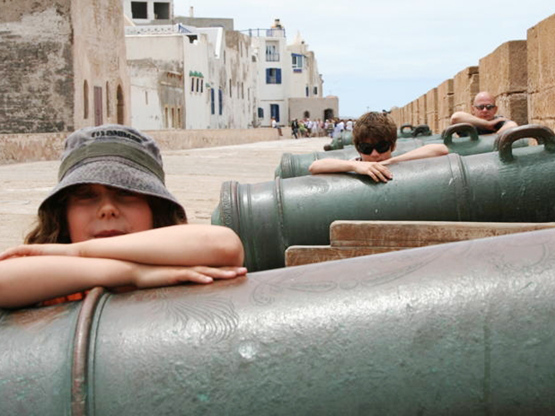 Two children and an adult leaning on cannons in Essaouira, Morocco