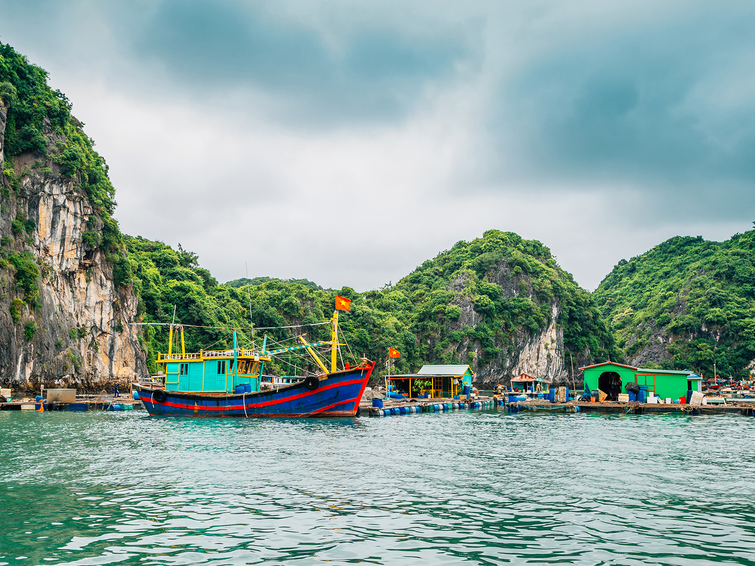 A village floating on the water in Lan Ha Bay with a fishing boat.