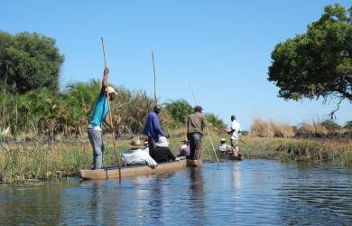 Travellers riding a traditional mokoro dugout canoe on the Okavango Delta in Botswana, a highlight o