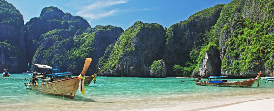 Traditional Thai boat resting on the calm ocean next to perfect white sand on Phi Phi Island