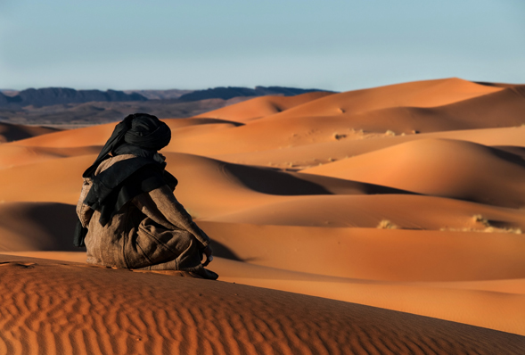 a man in traditional Berber dress sat looking out along the Sahara Desert