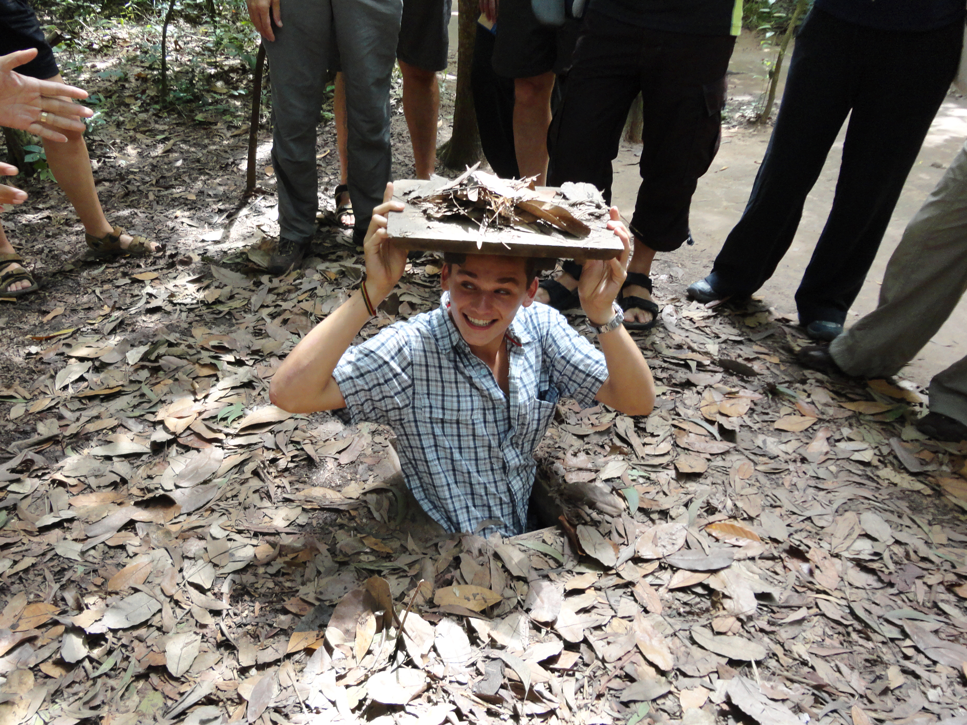 a man half way out of a small tunnel entrance in the ground.